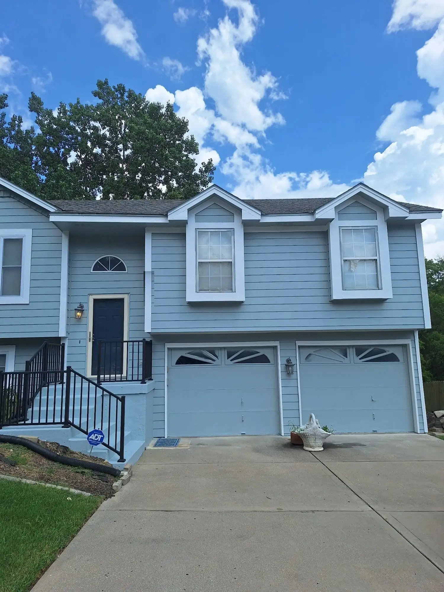 Two-storey house with pale blue siding, white trim and a black handrail beside the front steps