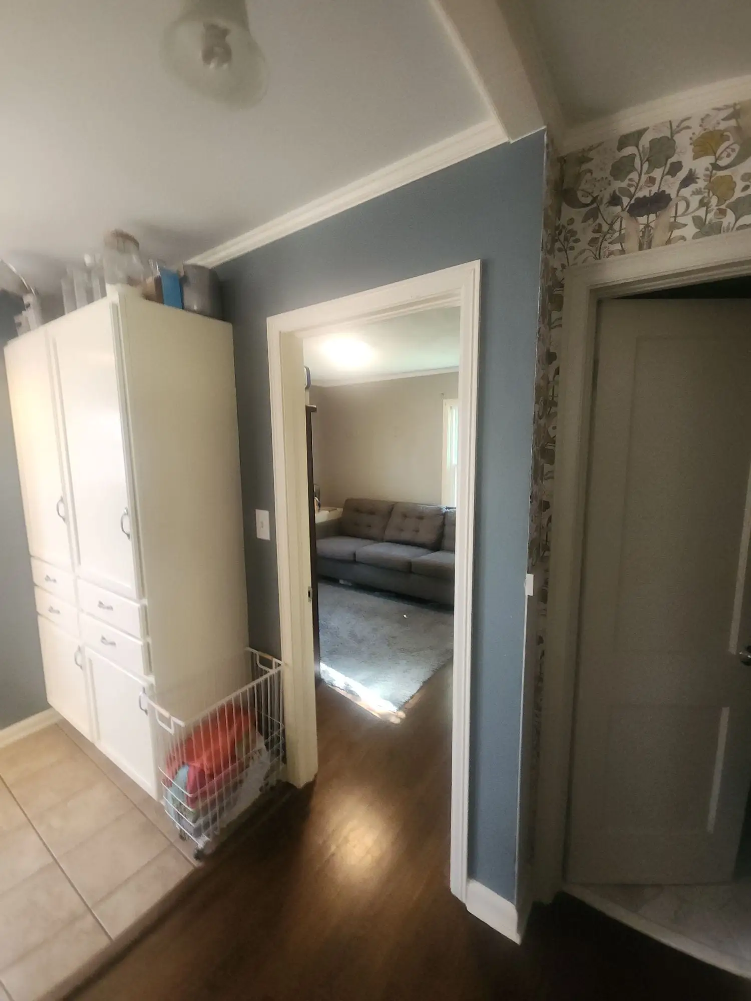Hallway painted in blue-grey with white trim, tall cabinets and a wood floor