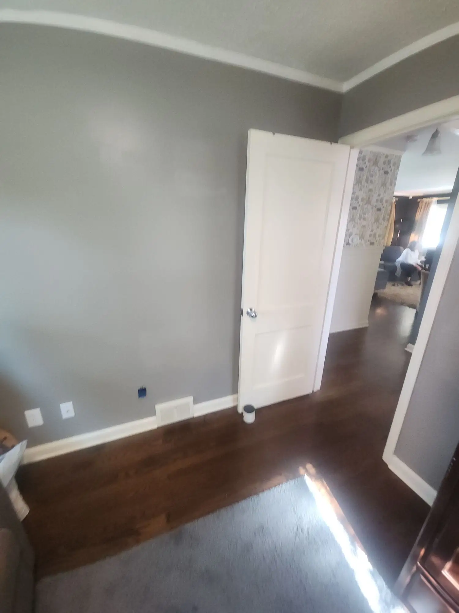 Room painted grey with crown moulding, a white door and a dark wood floor