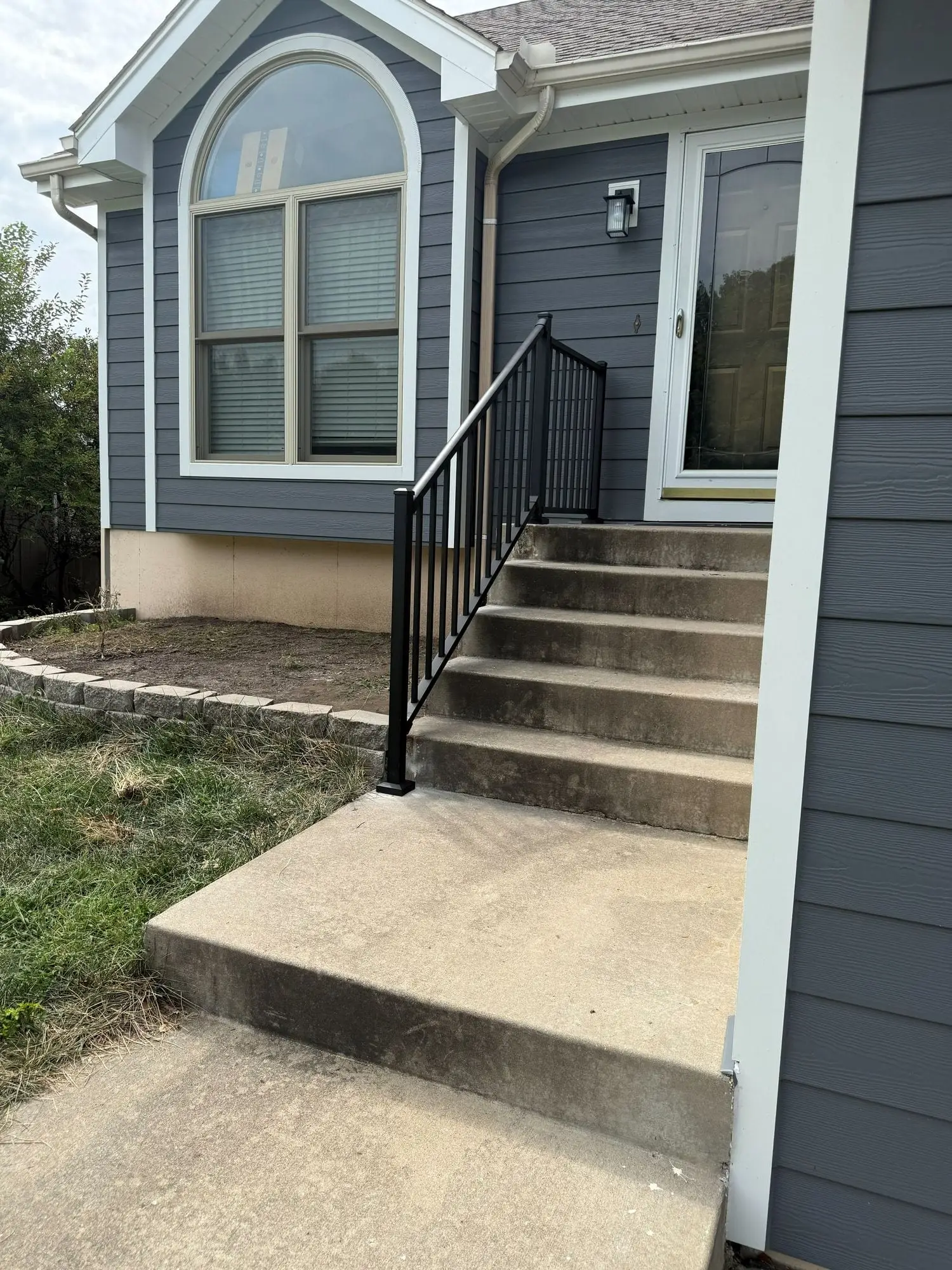 Concrete front steps and walkway with a new black metal handrail